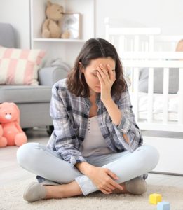 woman sitting on nursery floor holding his arm in front of her face as she is experiencing intrusive thoughts in postpartum