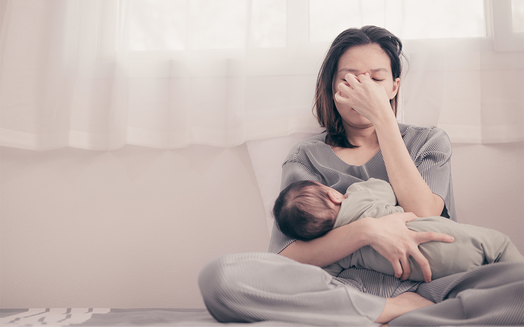 Mother holding a baby and pinching her nose while struggling with postpartum depression